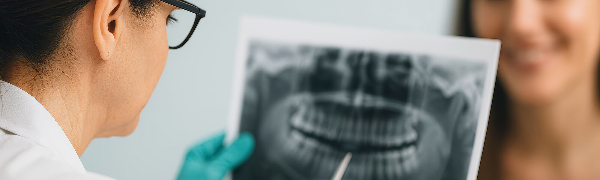 Zahnärztin mit Brille zeigt einer Patientin ein Röntgenbild und erklärt den Befund, Patientin lächelt.