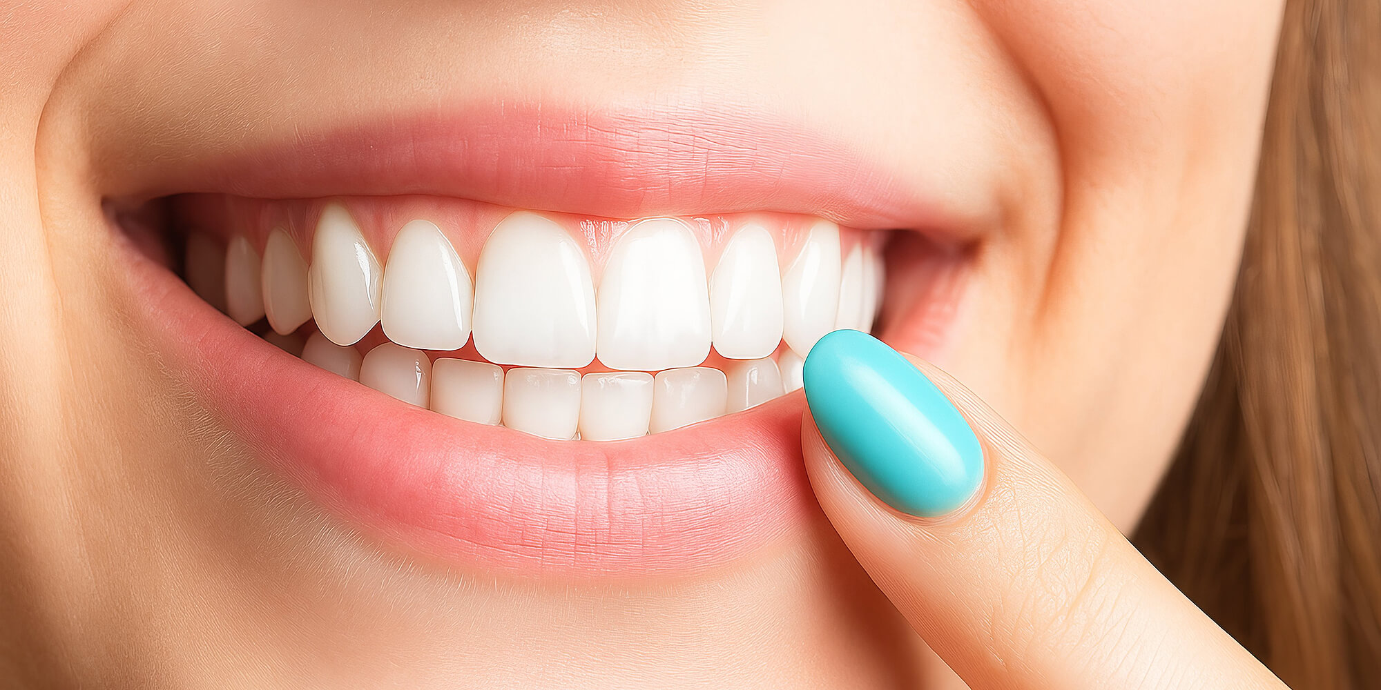 Nahaufnahme eines Lächelns mit weißen Zähnen, eine Hand mit türkisfarbenem Nagellack zeigt auf die Zähne.