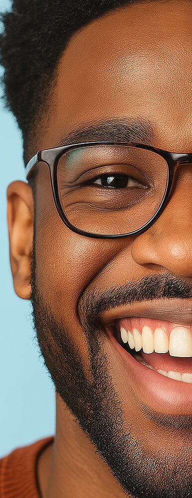 Lachender Mann mit Brille und Bart, Nahaufnahme der rechten Gesichtshälfte vor hellblauem Hintergrund.