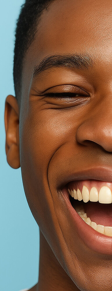 Nahaufnahme der linken Gesichtshälfte einer dunkelhäutigen Frau; sie lächelt freundlich und zeigt gepflegte weiße Zähne.