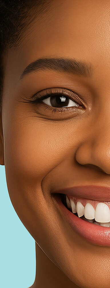 Nahaufnahme der linken Gesichtshälfte einer dunkelhäutigen Frau; sie lächelt freundlich und zeigt gepflegte weiße Zähne.