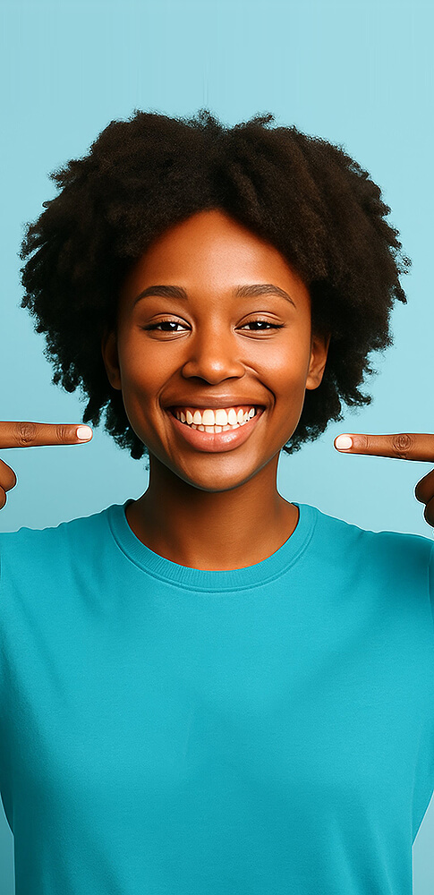 Lächelnde Frau mit lockigem schwarzen Haar, die mit beiden Zeigefingern auf ihr strahlendes Lächeln zeigt.