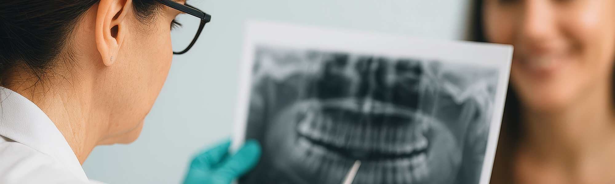 Zahnärztin hält ein Röntgenbild und erklärt der Patientin die Befunde