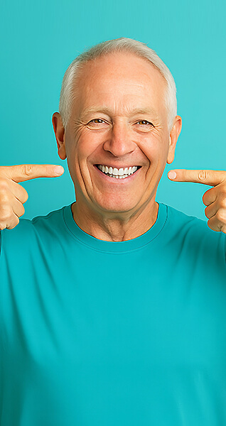 Älterer Mann lächelt und zeigt mit beiden Zeigefingern auf seine Zähne.