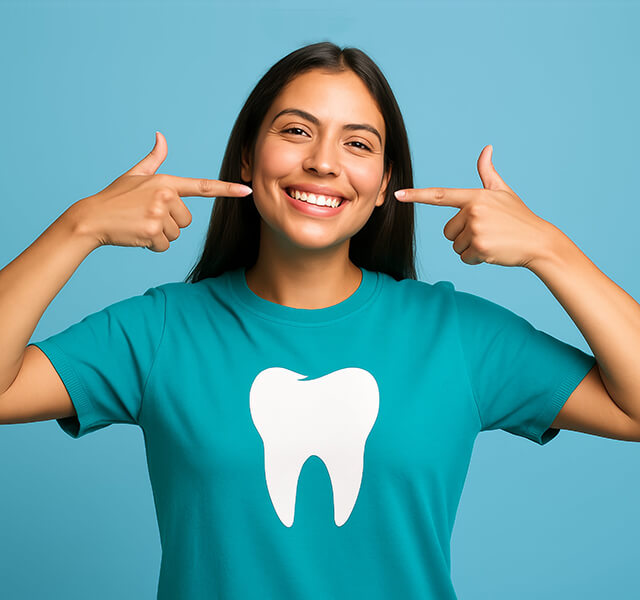 Lächelnde Person zeigt mit beiden Händen auf ihre Zähne, trägt ein T-Shirt mit Zahn-Symbol, blauer Hintergrund.