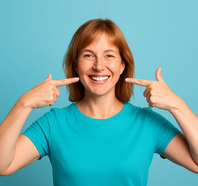Person in türkisfarbenem Shirt zeigt mit beiden Händen auf ihr Lächeln vor hellblauem Hintergrund.