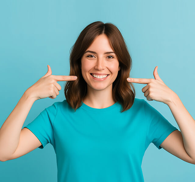 Lächelnde Person mit schulterlangen Haaren zeigt mit beiden Händen auf ihre Zähne, türkisfarbener Hintergrund.