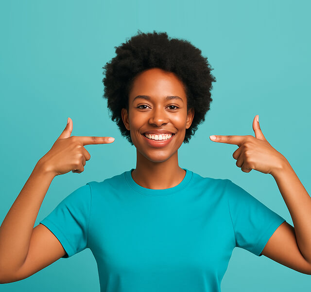 Lächelnde Person mit kurzem Afrohaar zeigt mit beiden Händen auf ihre Zähne, türkisfarbener Hintergrund.